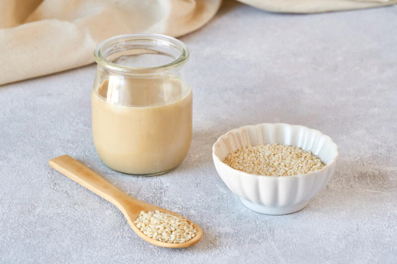 Glass jar with tahini and sesame seeds in a bowl on a table