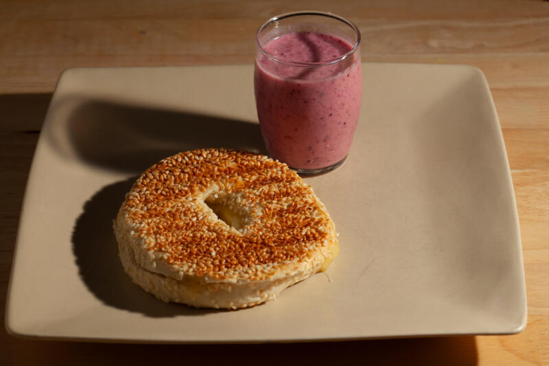 A quick homemade late night snack featuring sliced sesame bagel toasted with cheddar cheese right out of the sandwich press, served with a cup of freshly made mixed berry smoothie