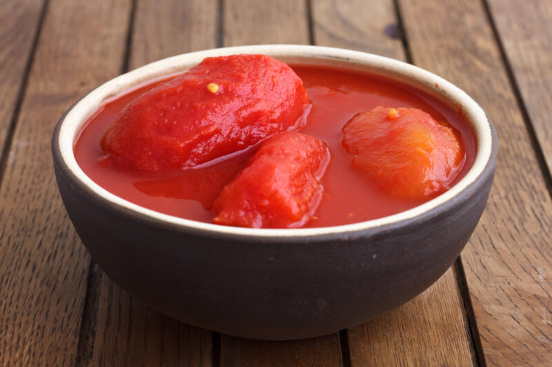 Whole canned tomatoes in a white ceramic bowl on the table