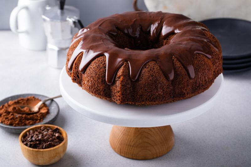 Chocolate bundt cake drizzled with chocolate ganache glaze on a serving plate in a kitchen