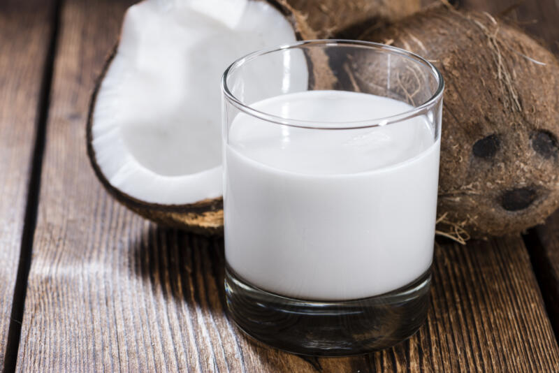 Coconut milk in a glass with fresh opened coconuts on the background 