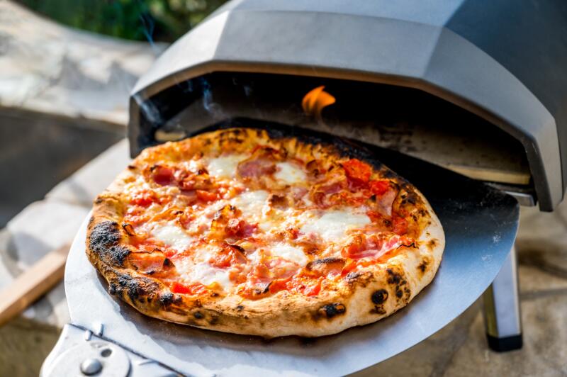 Taking out Margherita pizza out of portable gas pizza oven