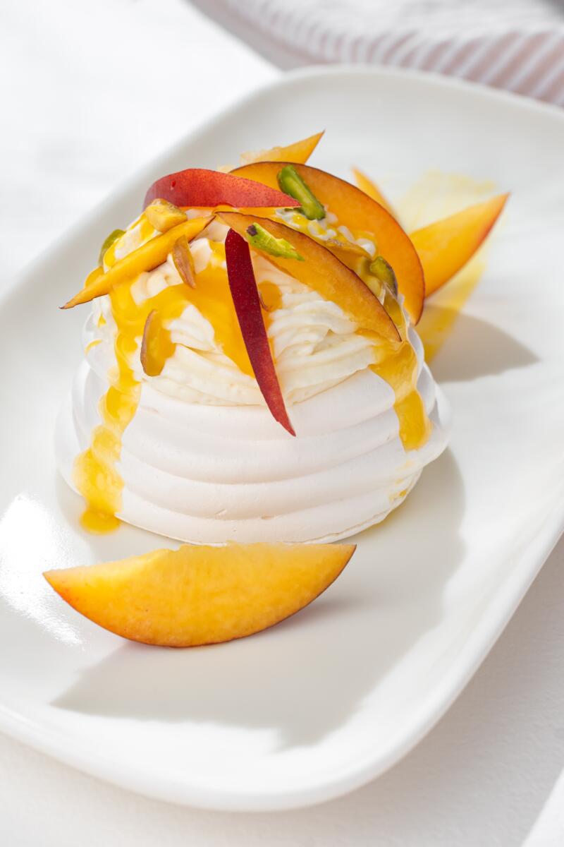 Pavlova meringue with passion fruit, nectarines, pistachio and whipped cream on a white plate