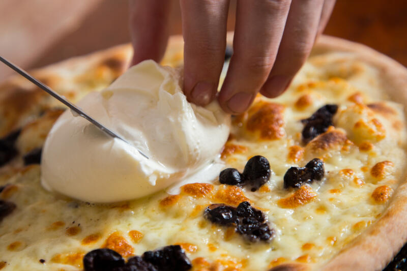 Slicing an Italian burrata on top of a pizza with cheese and black olives