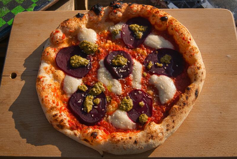 Freshly baked vegan pizza with beets, vegan mozzarella, tomato and pesto sauces