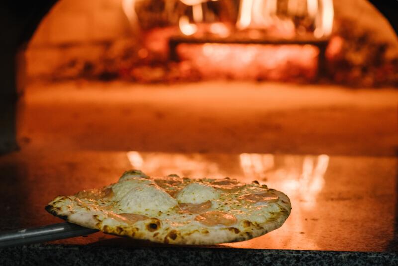 The chef is taking four-cheeses pizza out of wood-fired oven