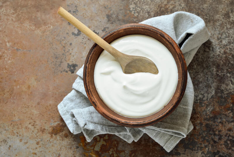 A bowl of sour cream with a wooden spoon in it on a rustic table
