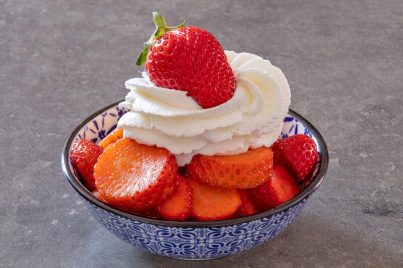 Bowl of cut strawberries with whipped cream in a small plate