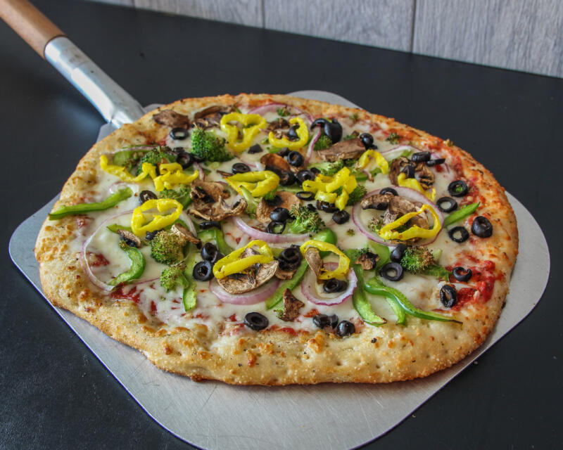 Veggie pizza on a pizza peel just out of wood-fired pizza oven