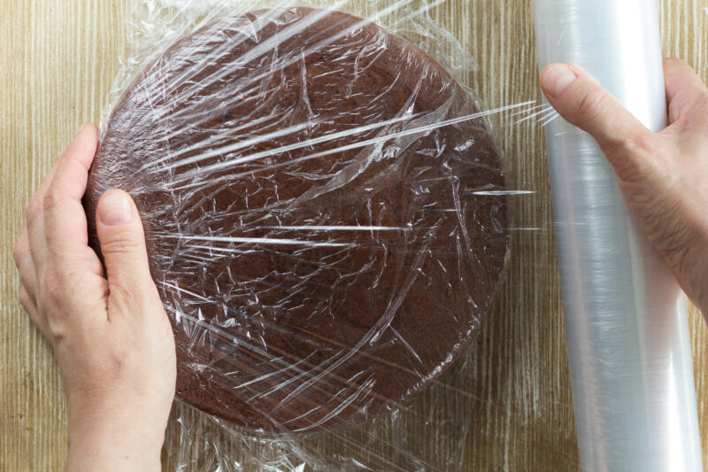 Top view of woman hand wrapping chocolate sponge cake in plastic for storing 