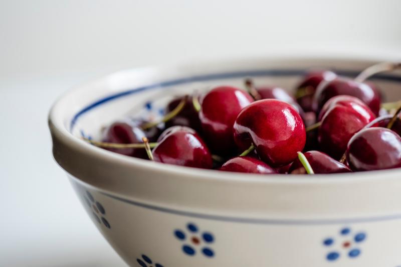 Sweet, ripe, dark red Bing cherries on stems are grouped in an off-white, round pottery bowl 