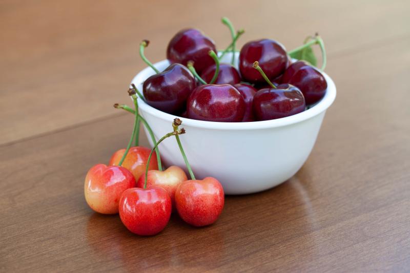 Red ripe cherries in a bowl and rainier cherries on table