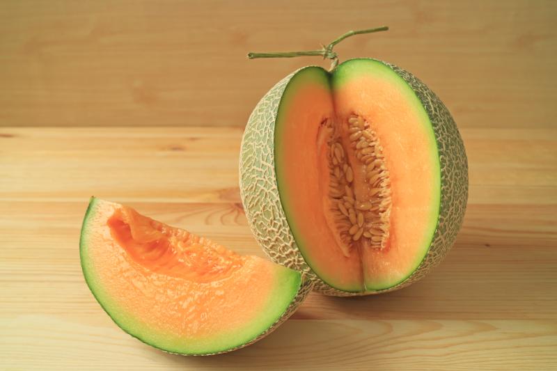 Juicy fresh ripe muskmelon chunk from the whole fruit isolated on wooden background