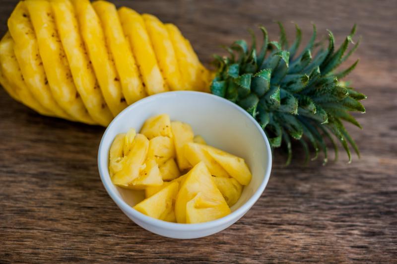 Peeled pineapple and ready slices to consume in a bowl on a wooden table