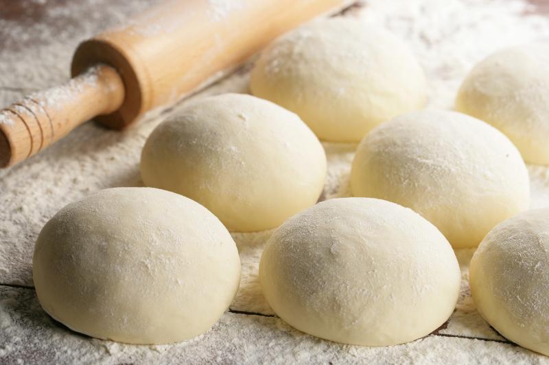 Preparation of homemade pizzas on kitchen table with a rolling pin