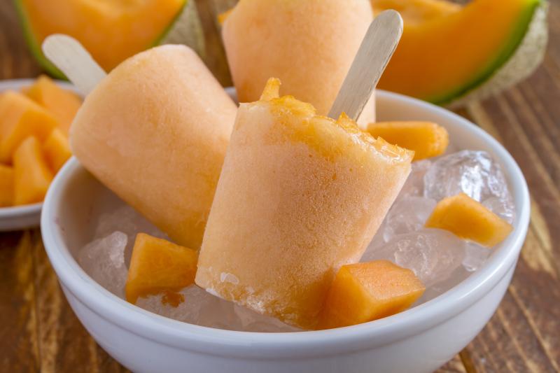 Homemade pureed frozen cantaloupe melon popsicles in white bowl with ice 