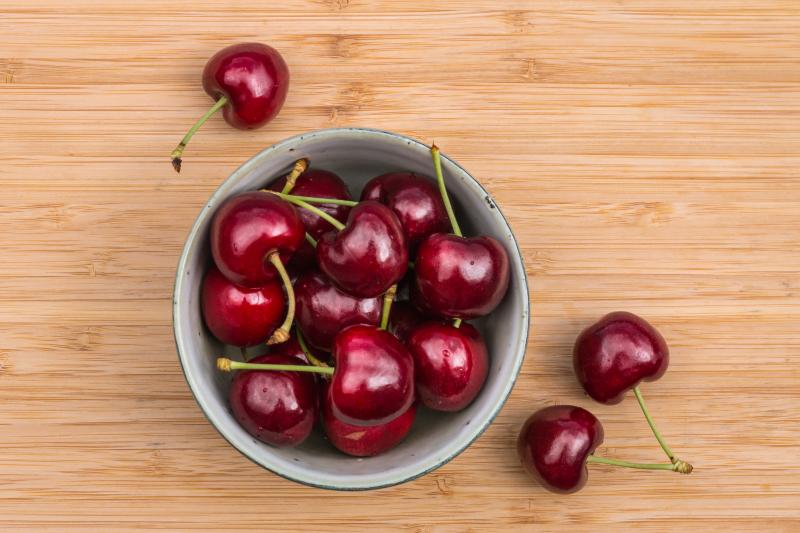 A porcelain bowl of Stella type of cherries on a wooden table