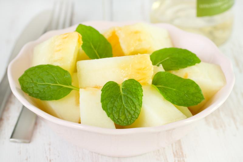 Melon cubes with mint leaves in a white bowl on a wooden table