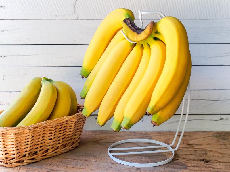 Yellow ripe banana hanging on hanger with white wooden background